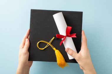 Ellerinde altın püsküllü siyah bir mezuniyet şapkası ve kırmızı kurdeleli bir diploma var.