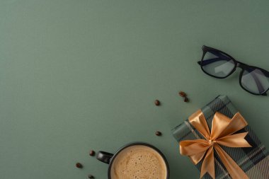 Sahnede altın kurdeleye sarılı bir hediye ve yeşil zemin üzerinde kahve ve bardaklar