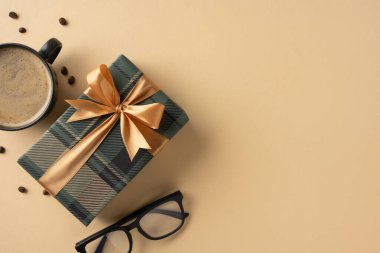 Kahve fincanı ve gözlüklerin yanına yerleştirilmiş altın bir fiyonklu dekoratif hediye kutusu.