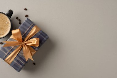 Kahve fincanının yanında altın kurdeleli mavi ekose hediye kutusu, bej arka planda.