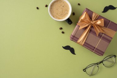 Yeşil yüzey üzerinde bir fiyonk, bir fincan kahve, gözlük ve dekoratif bıyıkla süslenmiş şık bir kompozisyon. Kutlama etkinlikleri ve erkeksi temalı kavramlar için idealdir.