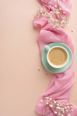 Pastel yüzeyinde kahve fincanı olan yumuşak ve samimi bir sahne, pembe kumaş aksanları ve küçük beyaz çiçeklerin narin dalları, sakinliği, sıcaklığı ve bahar havasını çağrıştırıyor.