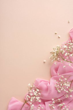 Bej bir yüzey üzerinde pembe kumaş ve beyaz çiçeklerin yer aldığı yumuşak ve zarif bir dikey kompozisyon