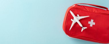 Minyatür bir uçağın yanına yerleştirilmiş kırmızı bir ilk yardım çantası. Seyahat güvenliğini simgeliyor.