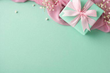 Pastel yeşili hediye kutusu pembe kurdeleli yeşil bir yüzey süslenmiş narin çiçeklerle