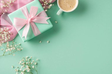 Pastel renkli hediye kutusu çiçeklerle çevrili bir kurdeleyle süslenmiş ve yeşil arka planda bir kahve fincanı var. Özen, kutlama ve düşünceli hediyeleri temsil eden bir kompozisyon.