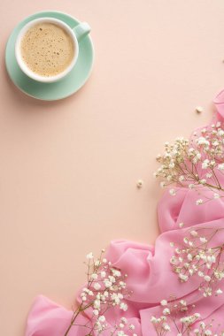 Süslü çiçekli yeşil bir fincanda servis edilen sıcak kahve ve dikey pastel yüzeyde kumaş.