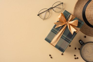 Altın kurdeleli hediye kutusu, bardaklar, kahve fincanı ve arka planda düzenlenmiş şapka.