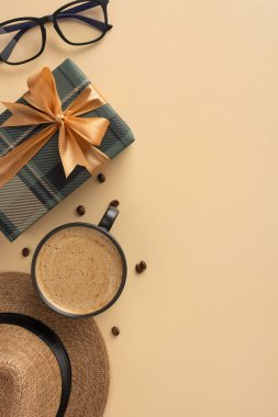 Açık bej bir yüzeye yerleştirilmiş kahve fincanı, hediye kutusu, gözlük ve hasır şapka içeren şık bir dikey kompozisyon.