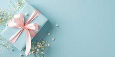 Mavi arka planda küçük çiçeklerle süslenmiş pembe kurdeleli şık bir hediye kutusu.