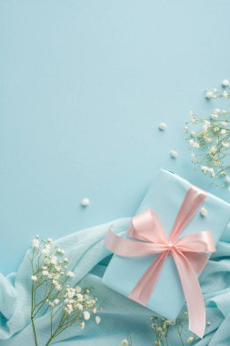 Yumuşak kumaşlar ve narin çiçeklerle çevrili pembe bir kurdeleyle sarılmış şık dikey bir hediye.