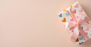 Sade bej arka planda pembe kurdeleli hediye kutusu, kalp desenli ambalaj, kutlama ve hediye için ideal, Sevgililer Günü gibi temalar için uygun.