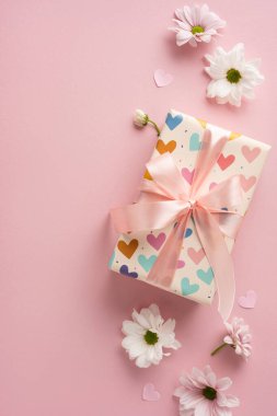 Kalp desenli dikey kağıda sarılı bir hediye kutusu, beyaz çiçeklerle çevrili bir kurdeleyle.