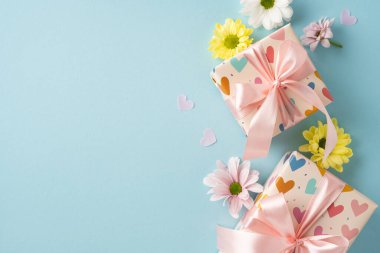 Renkli çiçeklerle çevrili, kalp tasarımı ve pembe fiyonklu iki paket hediye kutusu.