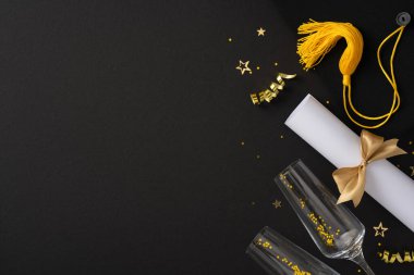 Kep, diploma, şampanya bardakları ve altın süslemeler içeren mezuniyet masası düzenlemesi.