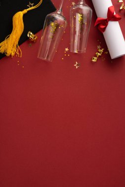 Dekoratif kırmızı dikey yüzey üzerine parlak gözlüklü mezuniyet şapkası ve rulo diploması kutlama öneriyor.