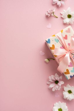 Kalp desenli hediye kutusu, pembe kurdele, papatyalar ve dikey pembe arka planda kalpler.