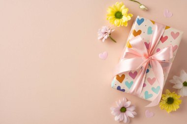 Yay ve renkli kalplerle süslenmiş bir hediye kutusu. Tarafsız bir yüzeyde çiçeklerle çevrili.