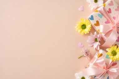 Yumuşak yüzeyde papatyalar ve pastel dekorlarla çevrili pembe kurdelelerle süslenmiş bir hediye.