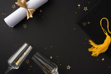 Diploma, altın püskül, iki şampanya bardağı ve siyah bir yüzeye yerleştirilmiş altın konfeti içeren mezuniyet temalı bir düzenek.