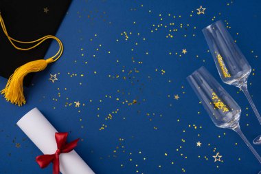 Mezuniyet şapkası, kurdeleli diploma, mavi arka planda şampanya bardakları ve altın konfetilerin yer aldığı kutlama kurulumu, başarıları, başarıları ve şenlikli anları simgeliyor.