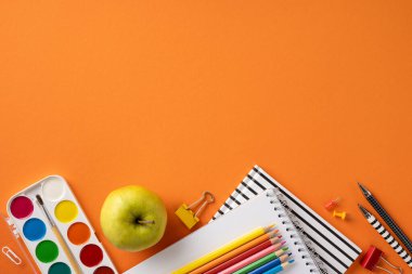 Sanat malzemeleri, kırtasiye malzemeleri ve turuncu arka planda bir elma içeren okul konseptine geri dönelim.