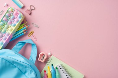 Çeşitli okul malzemeleri ve pastel pembe bir yüzeye yerleştirilmiş bir sırt çantası yaratıcılık ve organizasyonu çağrıştırıyor.
