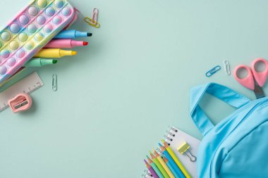 Okul malzemesi, okul temasına terfi eden sırt çantalı pastel bir arka planda.