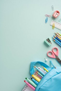 Renkli dikey kırtasiye gereçleri arasında bir defter, kalemler ve pastel renkli bir yüzey üzerinde sergilenen mavi bir sırt çantası etrafında düzenlenmiş bir cetvel var.