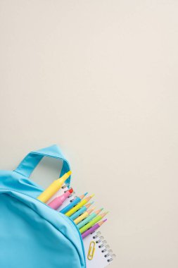 Öğrenmek için sırt çantasına dizilmiş renkli kalemler ve defterlerle okul asgari malzemesi.