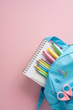 Okula dönüş sezonunu ve öğrencilerin organizasyonunu sembolize eden yumuşak pembe arka planda mavi bir sırt çantasıyla düzenlenmiş kalem, kalem ve makas da dahil olmak üzere okul dikey malzemeleri.