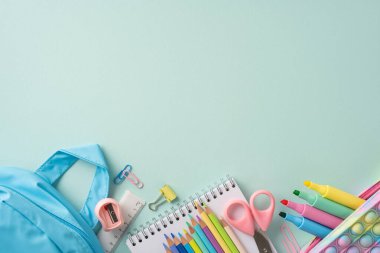 Yumuşak yeşil bir yüzeye sanatsal olarak yerleştirilmiş kalemler, keçeli kalemler ve defterler gibi renkli okul eşyalarının bir koleksiyonu.