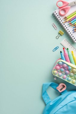 Makas, kalem, fosforlu kalem, cetvel ve sırt çantası da dahil olmak üzere pastel bir yüzeye yerleştirilmiş dikey malzemeler.