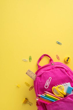 Canlı pembe bir sırt çantasından çıkan renkli yatay okul malzemeleri, okula hazırlık ve yaratıcılığı temsil eden neşeli sarı bir arka plana yerleştirilmiş.