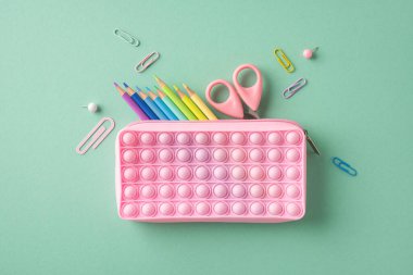 Pastel yüzeyinde canlı bir kırtasiye bulunan pembe bir kalem kılıfının yaratıcı düzenlemesi.