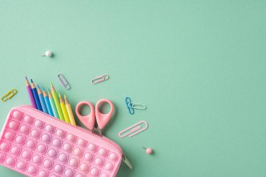 Renkli kalemler, makas ve ataçlar. Masada duran pembe bir çanta ile düzenlenmiş.