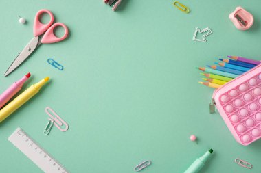 Açık yeşil bir yüzeye düzgün yerleştirilmiş çeşitli renkli okul malzemelerinin üst görüntüsü