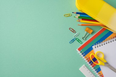 Kalemler, ataçlar ve defterler de dahil olmak üzere renkli okul malzemeleri.