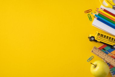Okul gereçleri, kitaplar, kalemler ve parlak sarı arka planda bir oyuncak otobüs de dahil.