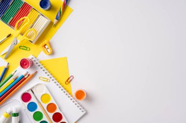 Masadaki boya, kalem, makas, kağıt ve ataçlar da dahil olmak üzere çeşitli okul malzemeleri.