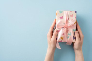 Kalp tasarımı hediye kağıdı ve kurdeleyle güzelce sarılmış bir hediyeyi tutan bir el. Bu resim, basit ve zarif bir şekilde hediyeleri, aşkı, kutlamaları ve özel durumları tasvir eder.