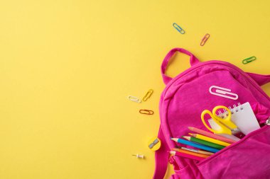 Parlak sarı bir arka plana yerleştirilmiş okul malzemelerini içeren pembe bir sırt çantası.