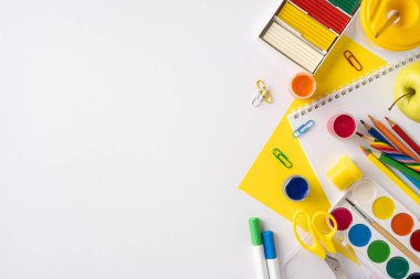 Beyaz arka planda renkli kalemler, defterler ve sanat materyalleri, eğitim ve yaratıcılığı çağrıştıran okul kırtasiyesinin yaratıcı düzeni