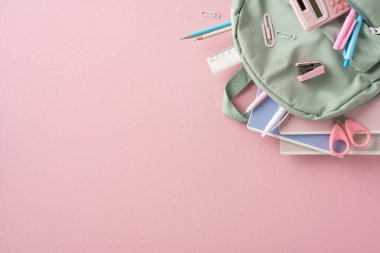 Pembe bir yüzeye yerleştirilmiş sırt çantasıyla birlikte düzgünce düzenlenmiş okul esasları.