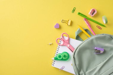 Kalemler, makas ve sarı arka planda sergilenen bir defter de dahil olmak üzere çeşitli okul malzemeleri.