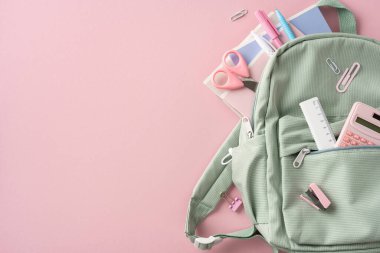 Yeşil okul sırt çantası yumuşak pembe arka plana karşı rengarenk sabit nesneler ile düzenli