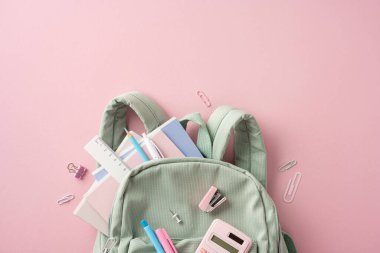 Açık yeşil kadife kadife çanta. Renkli okul malzemeleriyle dolu. Pembe bir arka fona yerleştirilmiş.