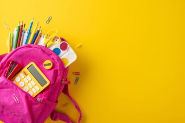 Renkli okul malzemeleri parlak pembe bir sırt çantasından dökülüyor, okula dönmeye hazır olduğunu gösteriyor.