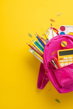 Okul malzemeleriyle dolu parlak pembe bir sırt çantası. Hesap makinesi, kalem ve kalemler de dahil.