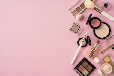Çeşitli kozmetik ürünler, fırçalar, göz farı ve rujlar, pembe arka fonda serili.